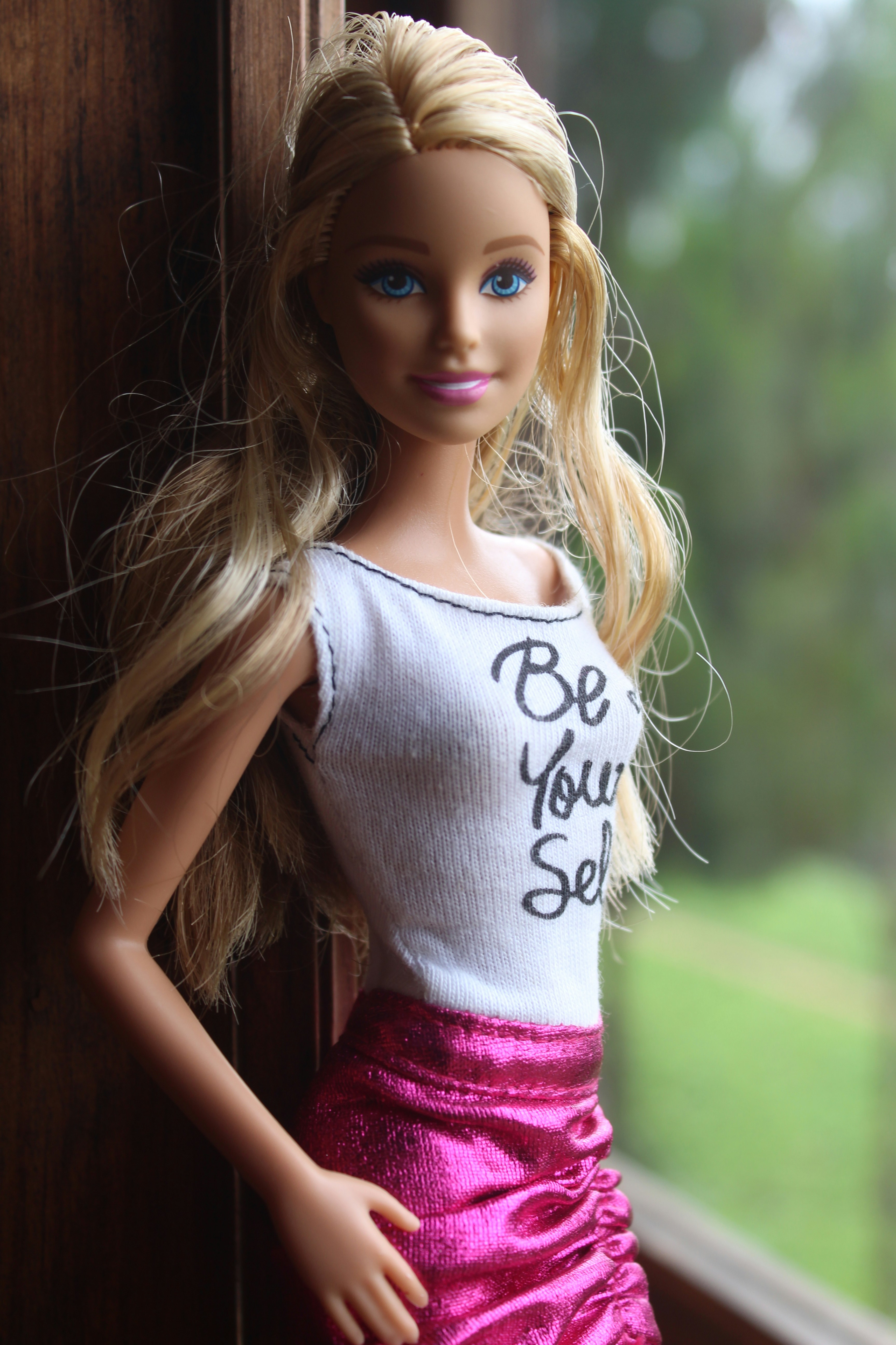 Photo by Sandra Gabriel, Barbie (doll) poses by a window wearing tank top that says Be Your Self